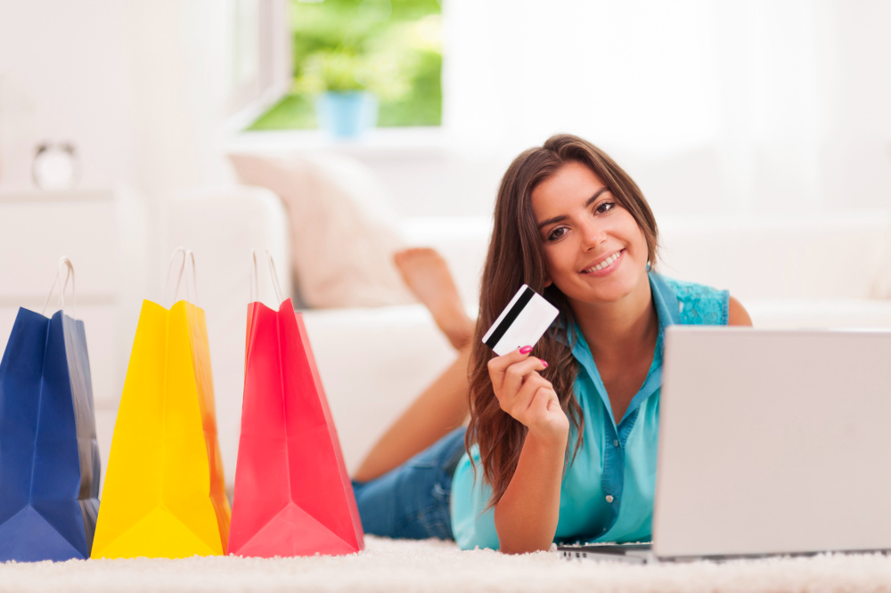 Mujer comprando online con tarjeta de crédito y portátil rodeada de bolsas