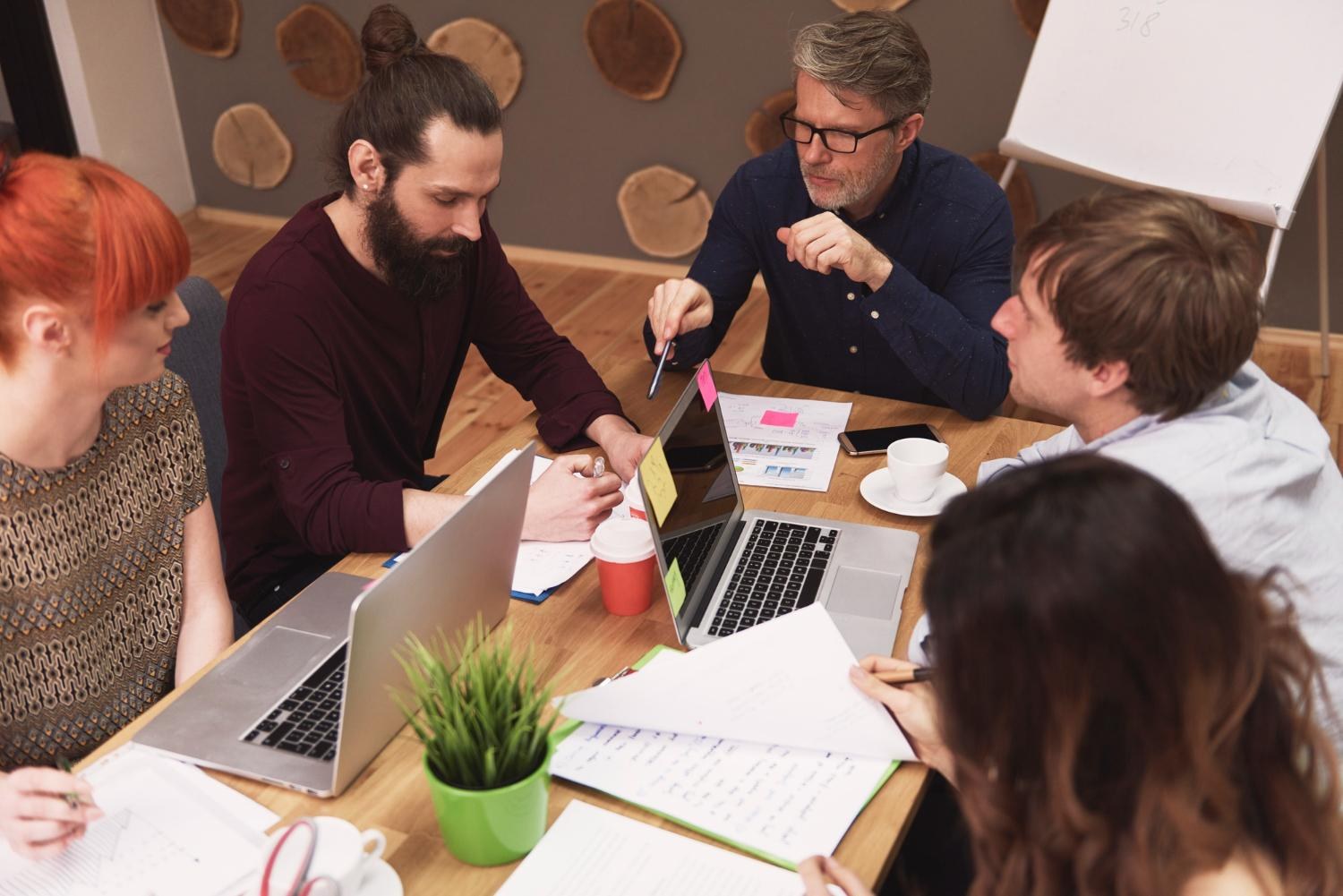 Equipo de una agencia creativa trabajando junto a varios portátiles con propuestas y documentos de cliente